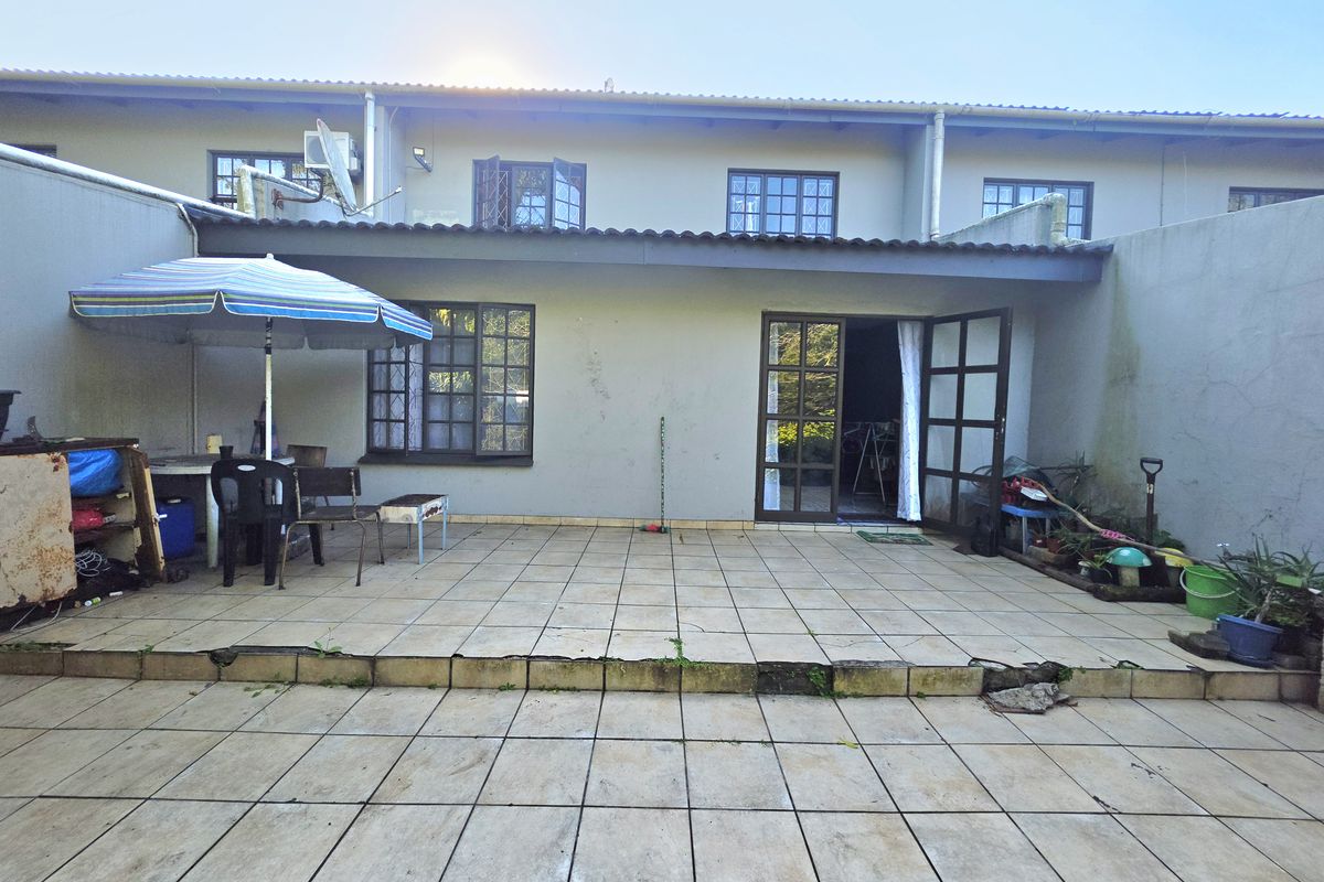 Rear exterior view of an apartment featuring a tiled patio area, covered veranda, and access through french doors with lattice-style windows.