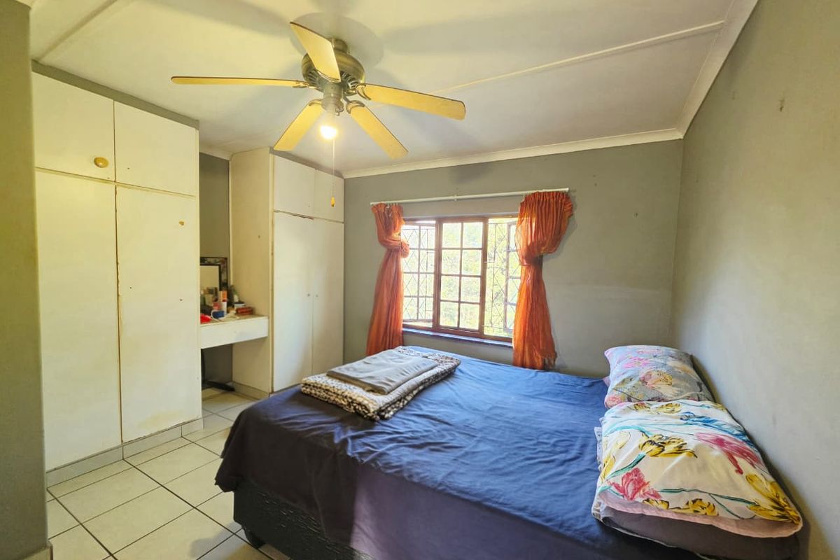 A functional bedroom featuring built-in cupboards, a ceiling fan, and tiled flooring, offering a practical layout with natural light through the window.
