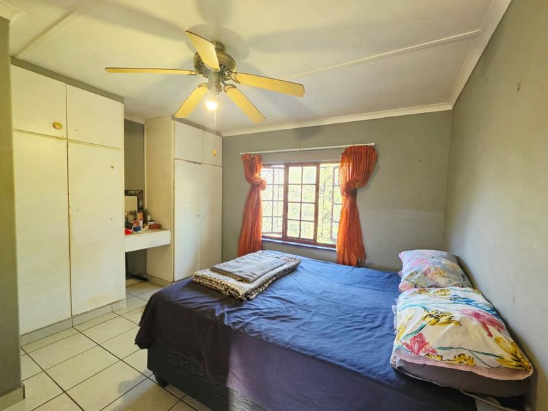 A functional bedroom featuring built-in cupboards, a ceiling fan, and tiled flooring, offering a practical layout with natural light through the window.