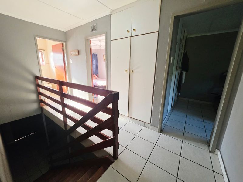 A functional upper-level hallway featuring tiled flooring, built-in storage cupboards, and a wooden staircase railing leading to the lower level.
