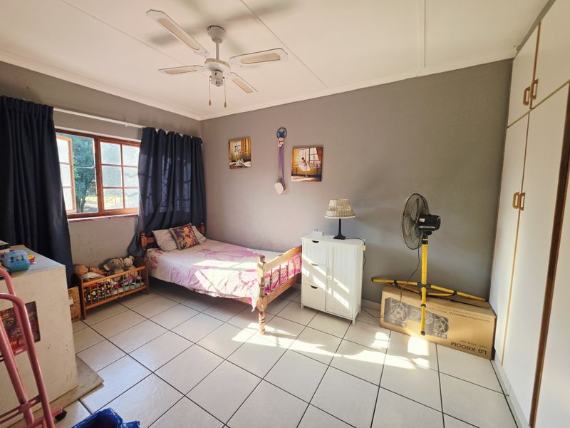 A functional bedroom featuring tiled flooring, a ceiling fan, and built-in cupboards, offering a practical space with natural light.