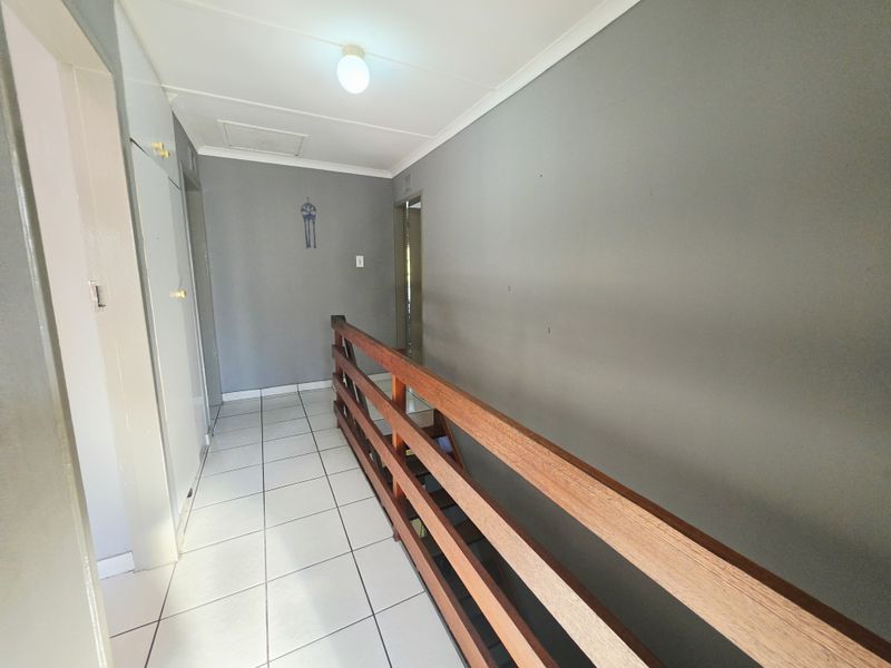 A bright, tiled hallway featuring a wooden balustrade overlooking the lower level and built-in storage cupboards.