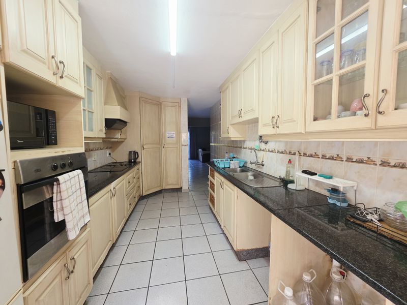 A functional galley-style kitchen featuring light-toned cabinetry, granite countertops, tiled flooring, and integrated appliances including an oven and hob.