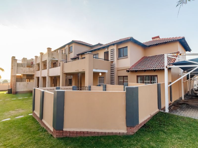Rear view of a multi-story apartment complex featuring private balconies, a shared garden area, and covered carport parking.