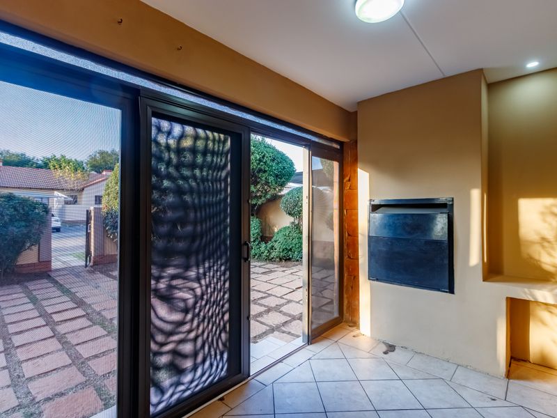 Covered patio area featuring a built-in braai, tiled flooring, and large sliding glass doors providing direct access to the garden.