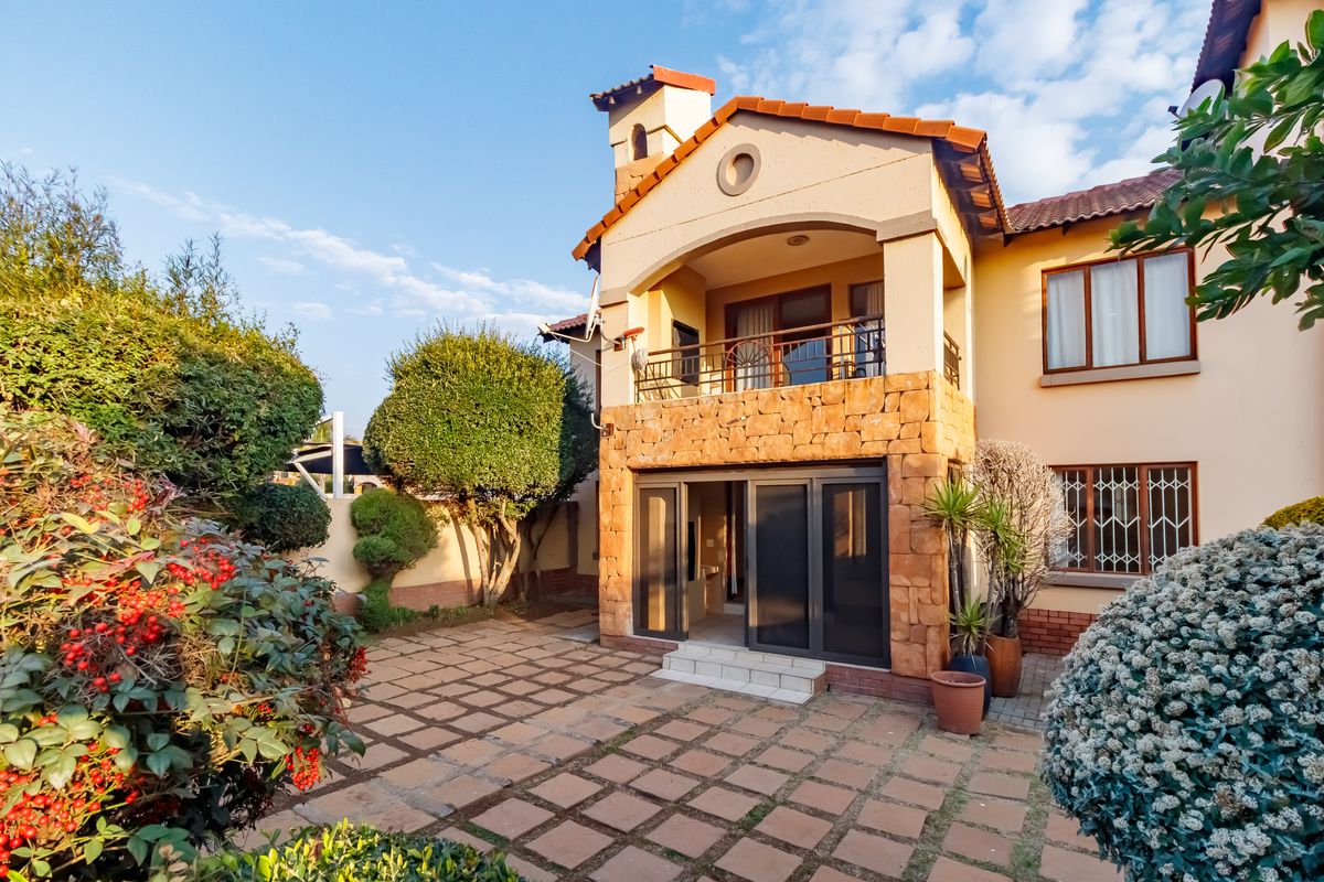Rear view of the property featuring a paved patio area, stone-clad facade, and an upper-level balcony with sliding door access.