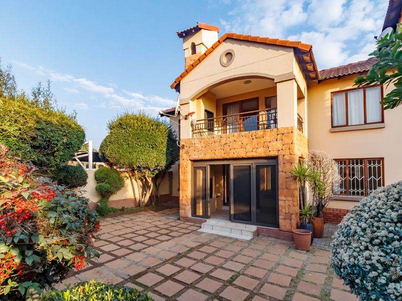 Rear view of the property featuring a paved patio area, stone-clad facade, and an upper-level balcony with sliding door access.