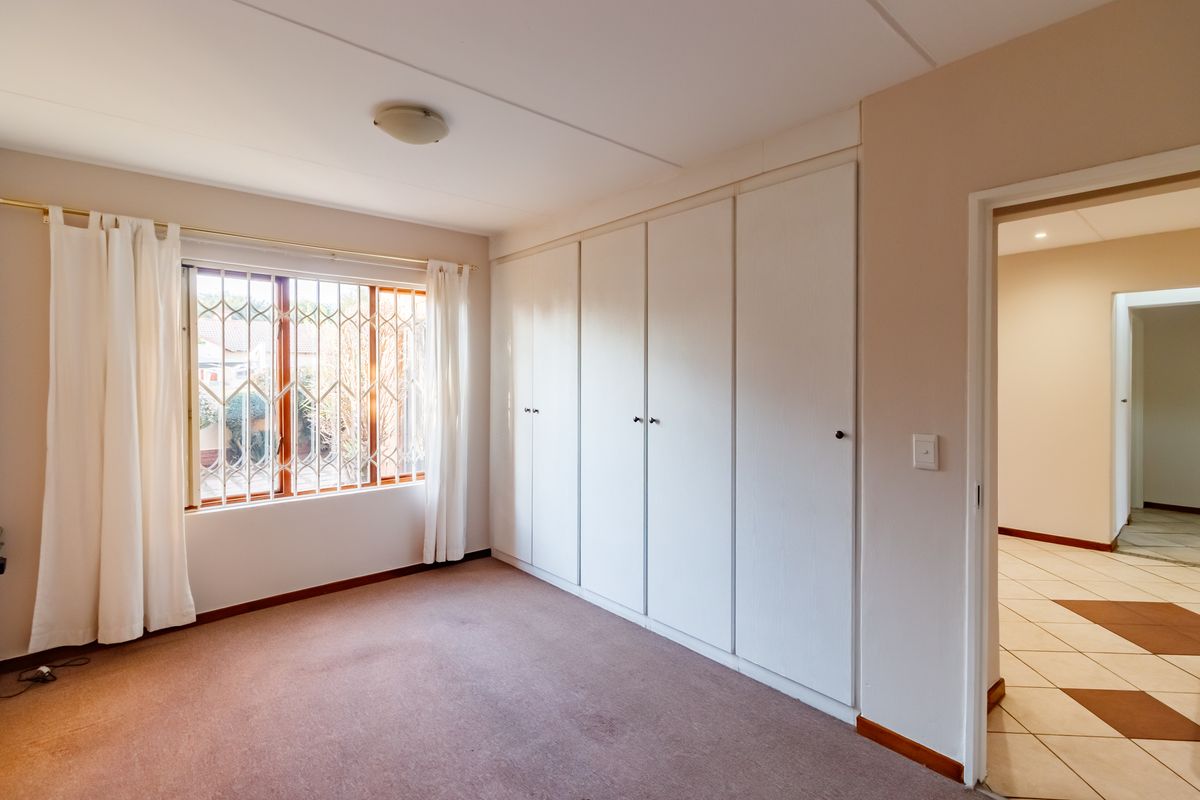 A spacious, empty bedroom featuring neutral walls, carpeted flooring, and extensive built-in cupboard storage, with a security gate on the window.