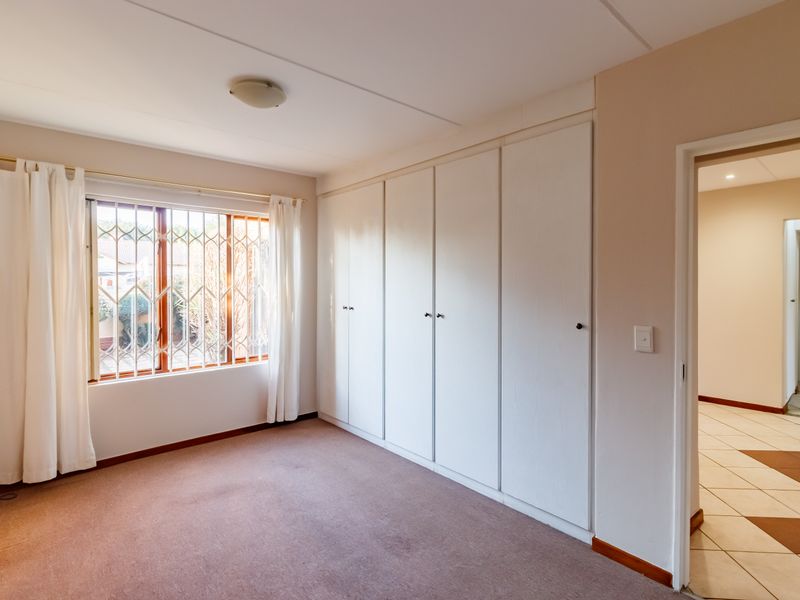 A spacious, empty bedroom featuring neutral walls, carpeted flooring, and extensive built-in cupboard storage, with a security gate on the window.