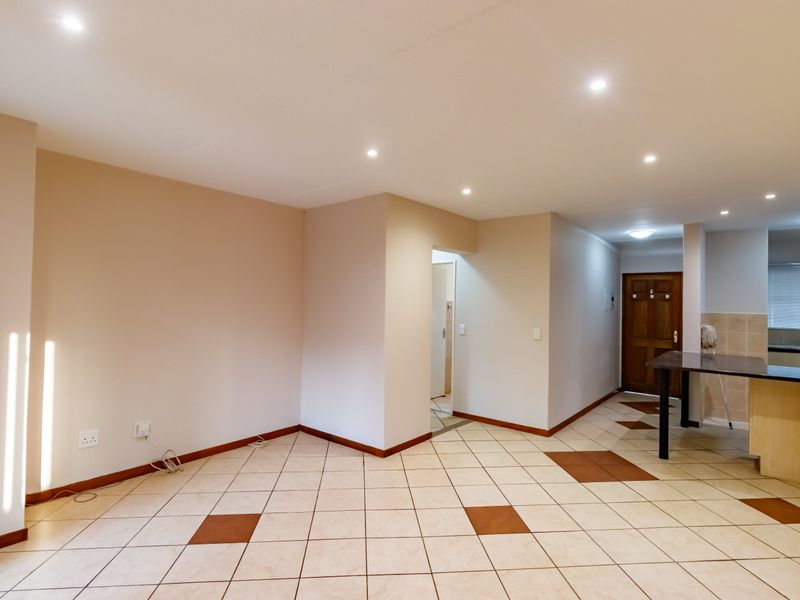 An open-plan living and kitchen area featuring neutral walls, tiled flooring with decorative accents, recessed lighting, and a breakfast bar counter.