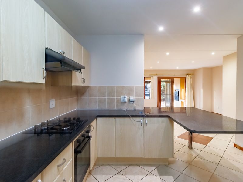 Open-plan kitchen featuring light wood cabinetry, dark stone countertops, gas hob, and built-in oven, flowing into an adjacent living area.