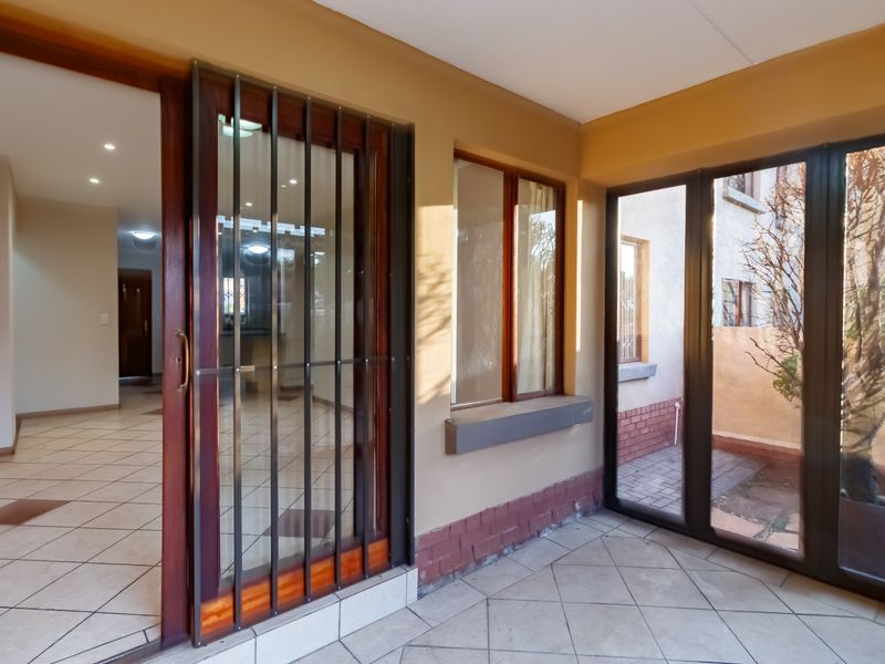 A covered patio area featuring tiled flooring, a secure sliding door entrance, and large windows overlooking a small rear courtyard space.