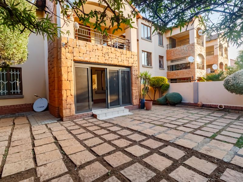 Rear view of the apartment building featuring a paved patio area, stone-clad facade, and sliding door access to the ground floor unit.