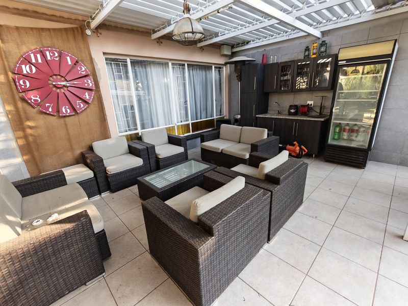 A spacious covered patio area featuring tiled flooring, a built-in kitchenette with cabinetry and sink, ideal for outdoor entertaining.