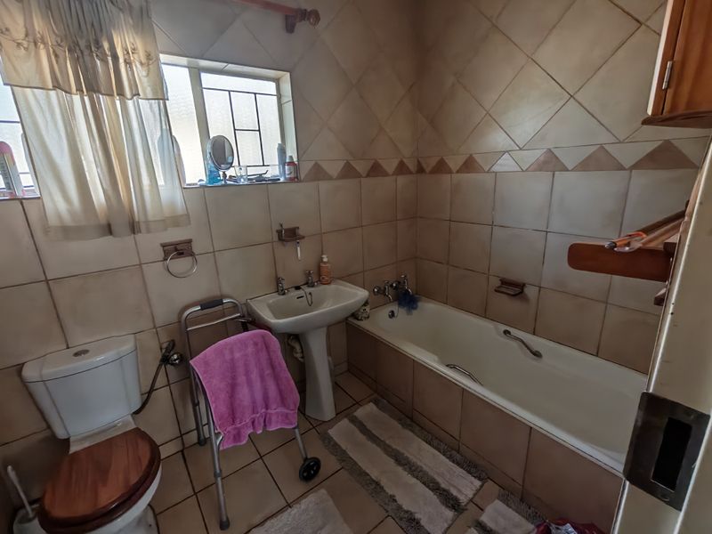 A dated bathroom featuring a pedestal basin, built-in bathtub, and full-height ceramic wall tiling, requiring cosmetic updates to modernize the space.