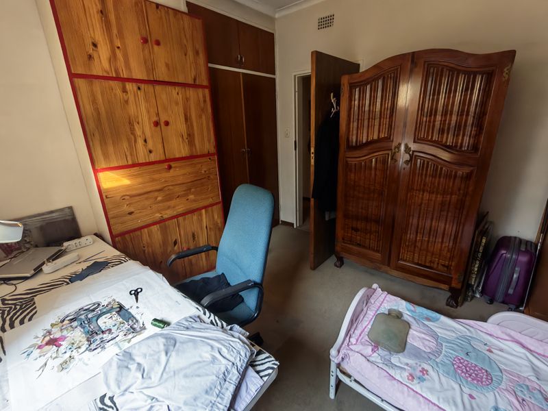 A bedroom featuring built-in wooden cupboards, ceiling cornicing, and carpeted flooring, offering potential for modernization and improved layout.