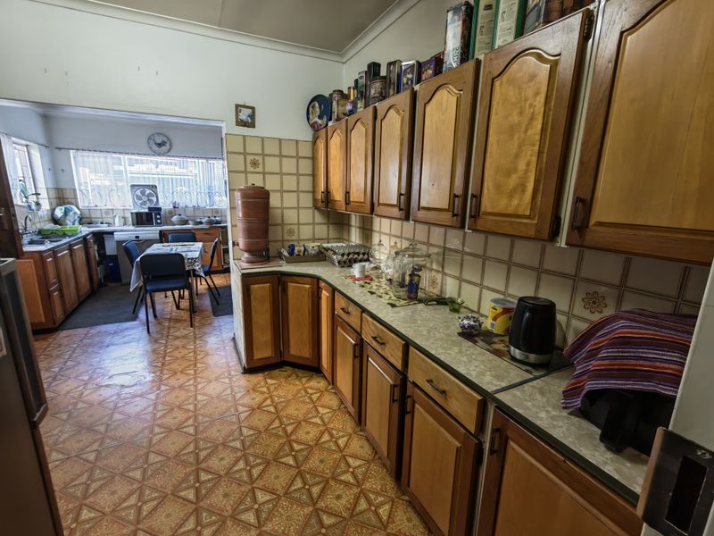 A functional kitchen featuring traditional wooden cabinetry, laminate countertops, and patterned vinyl flooring, offering a dated aesthetic with potential for modern renovation.