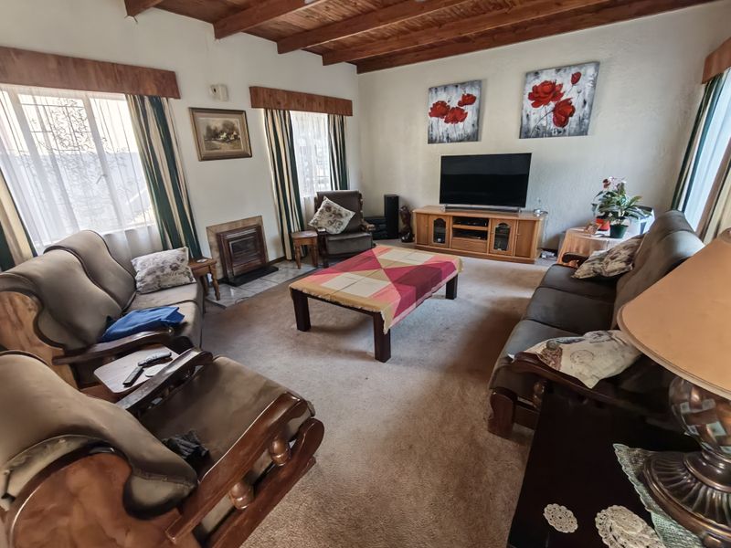 A cozy living room featuring exposed timber ceiling beams and a built-in fireplace with a tiled hearth.