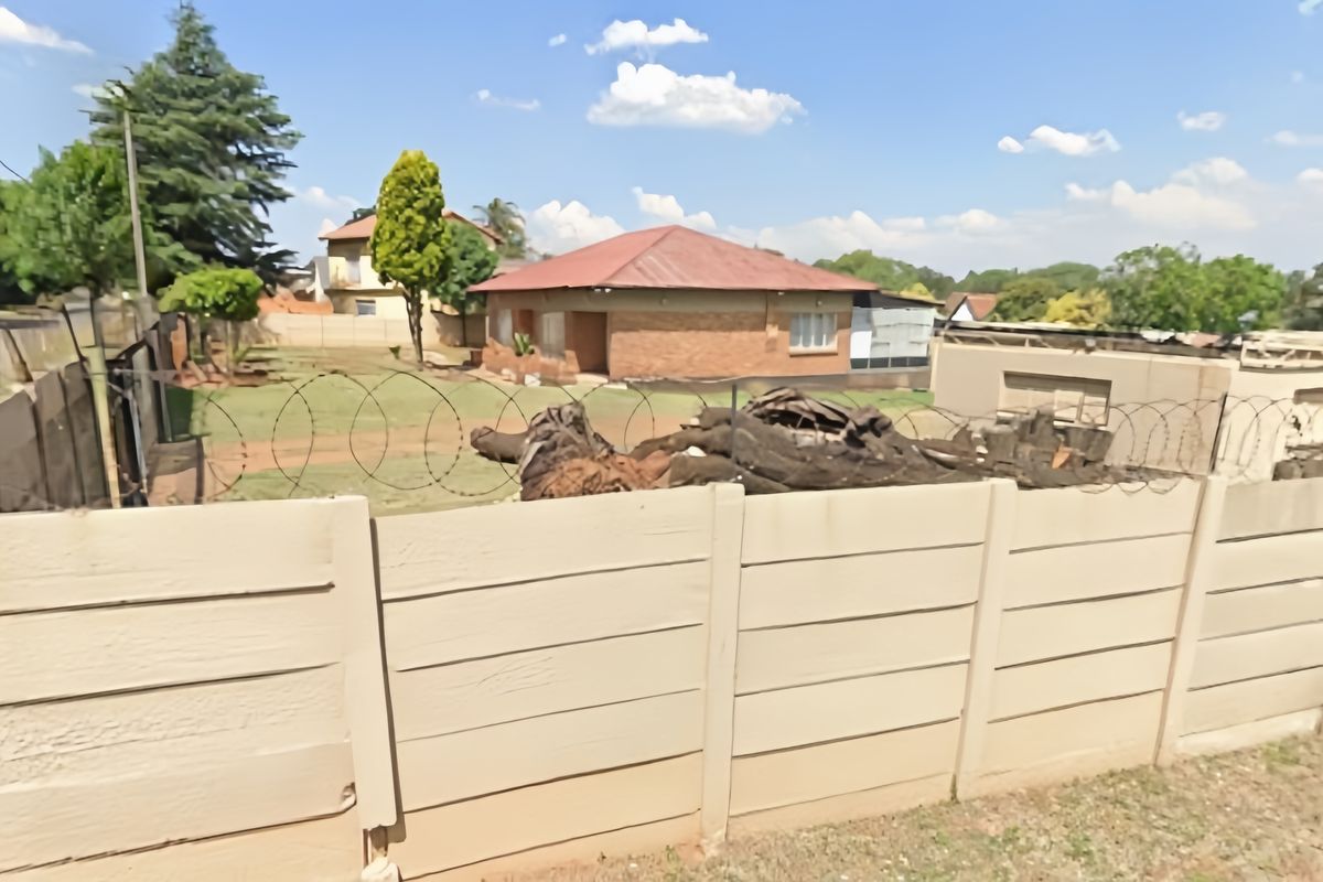 Rear view of a brick house featuring a precast concrete boundary wall with razor wire and an expansive yard area.