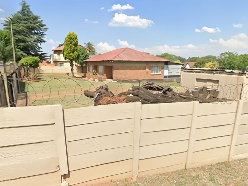Rear view of a brick house featuring a precast concrete boundary wall with razor wire and an expansive yard area.