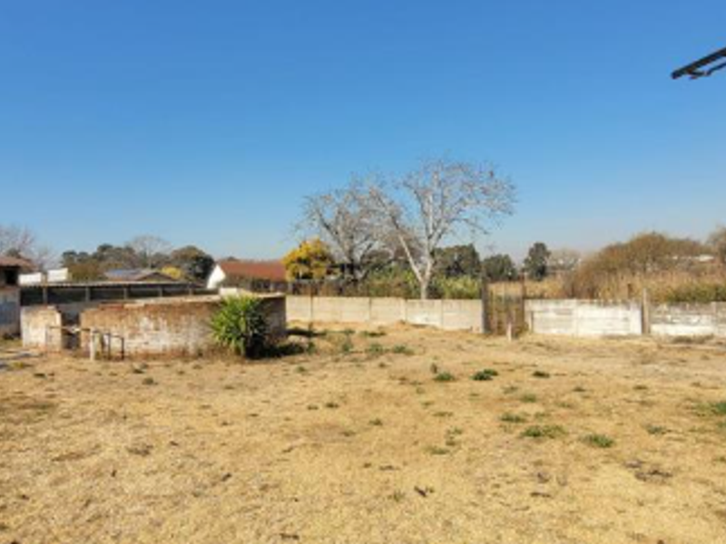A large, undeveloped rear yard area featuring a precast concrete boundary wall, a small brick structure, and a metal pole on a dry grass plot.