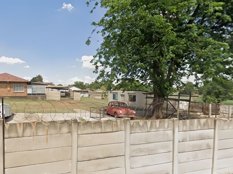 Rear exterior view of the property featuring a precast concrete boundary wall with razor wire, a concrete driveway, and a large mature tree.