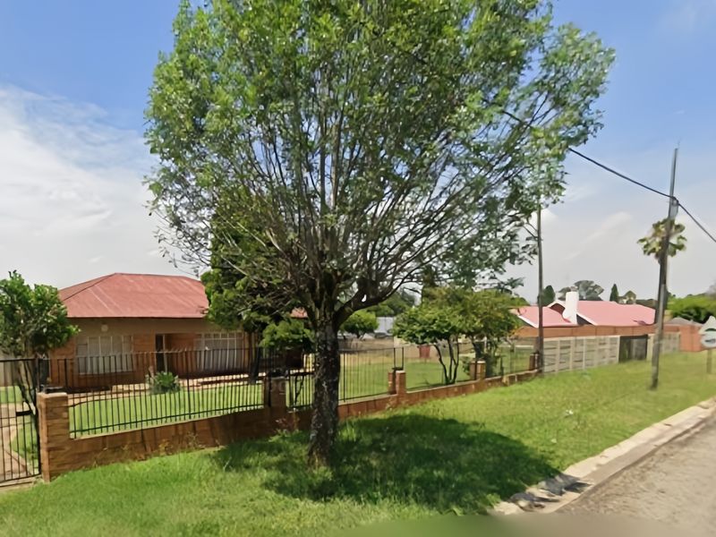A street-level view of a residential property featuring a brick facade, tiled roof, and a fenced front garden area.