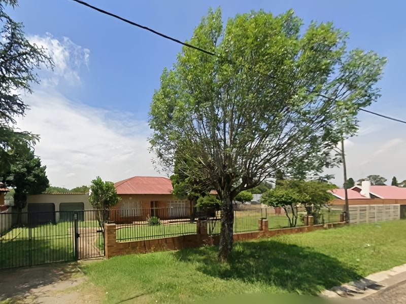 Front view of a single-story brick house featuring a tiled roof, enclosed by a metal fence and brick boundary wall with a gated entrance.