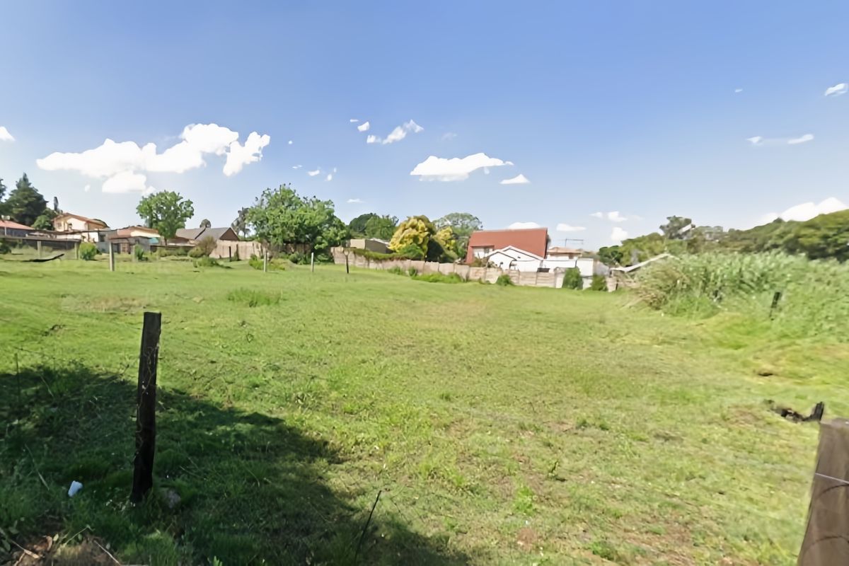 A large, open grassed plot of land enclosed by wire fencing, offering a clear view of the surrounding residential neighbourhood.