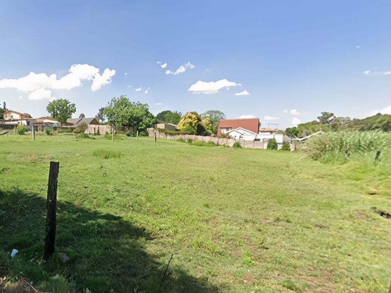 A large, open grassed plot of land enclosed by wire fencing, offering a clear view of the surrounding residential neighbourhood.