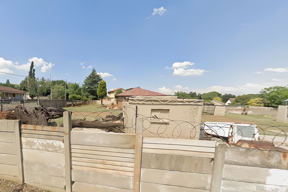Rear view of the property showing a precast concrete boundary wall with razor wire and a weathered outbuilding in the backyard.