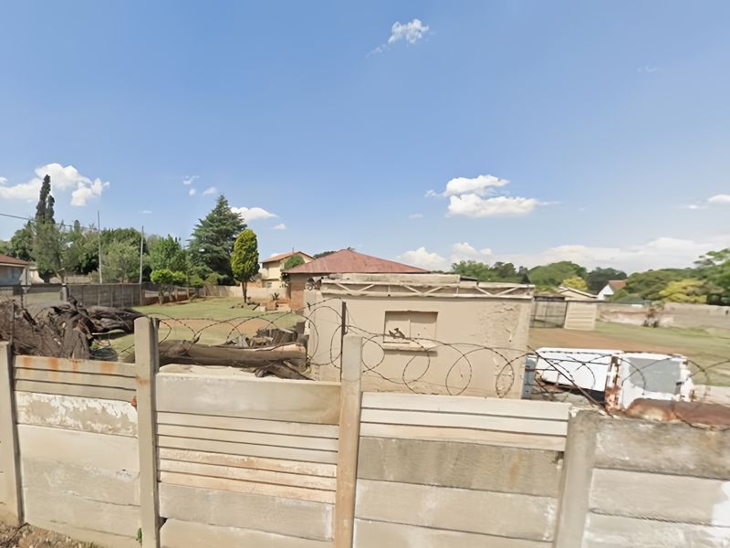 Rear view of the property showing a precast concrete boundary wall with razor wire and a weathered outbuilding in the backyard.
