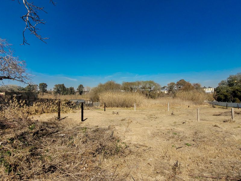 An undeveloped plot of land featuring dry grass, perimeter fencing, and concrete posts, offering a blank canvas for future landscaping or development.