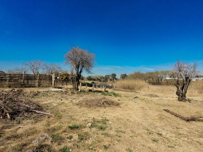 An expansive, undeveloped plot of land featuring dry grass, scattered trees, and perimeter fencing, offering potential for landscaping or future development.