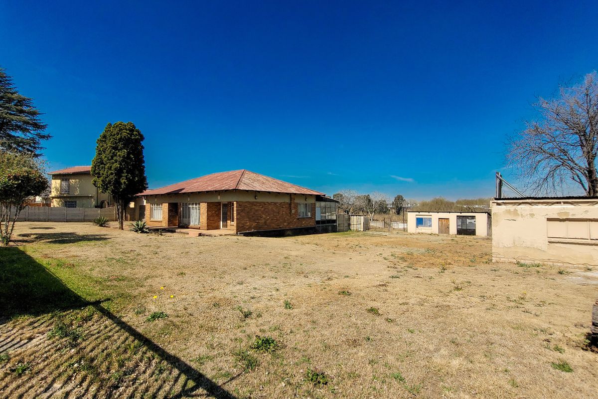 Rear view of a brick house featuring a corrugated metal roof, a large yard, and a separate outbuilding structure.