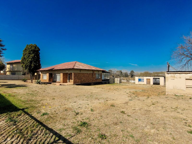 Rear view of a brick house featuring a corrugated metal roof, a large yard, and a separate outbuilding structure.