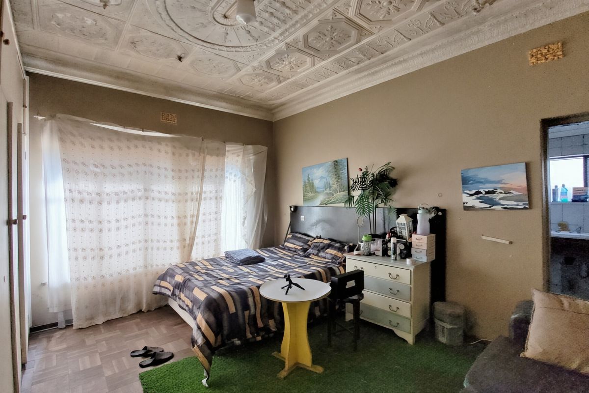 Spacious bedroom featuring a unique ornate pressed metal ceiling and classic parquet flooring, offering significant potential for renovation and modernization.