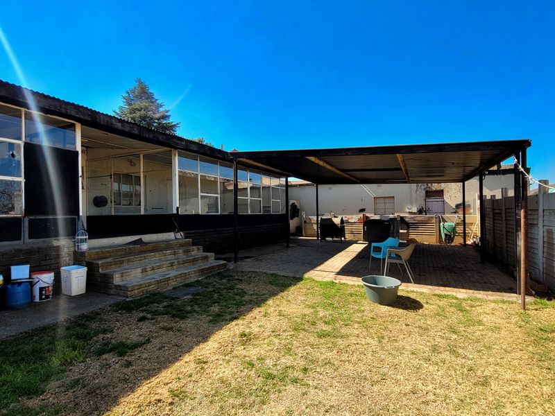 Rear exterior view featuring a large covered patio area with paved flooring, concrete steps, and a spacious backyard.