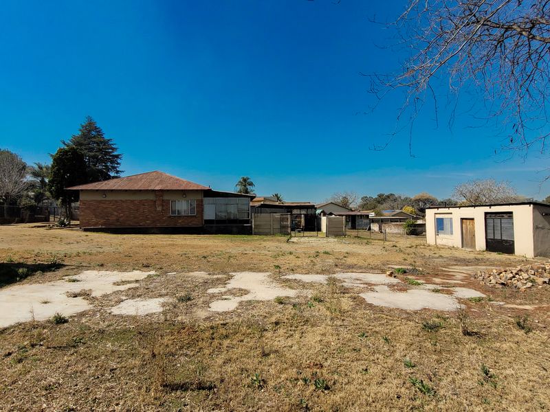 Rear view of the property showing a brick house, an outbuilding, and a large yard with a concrete slab area.