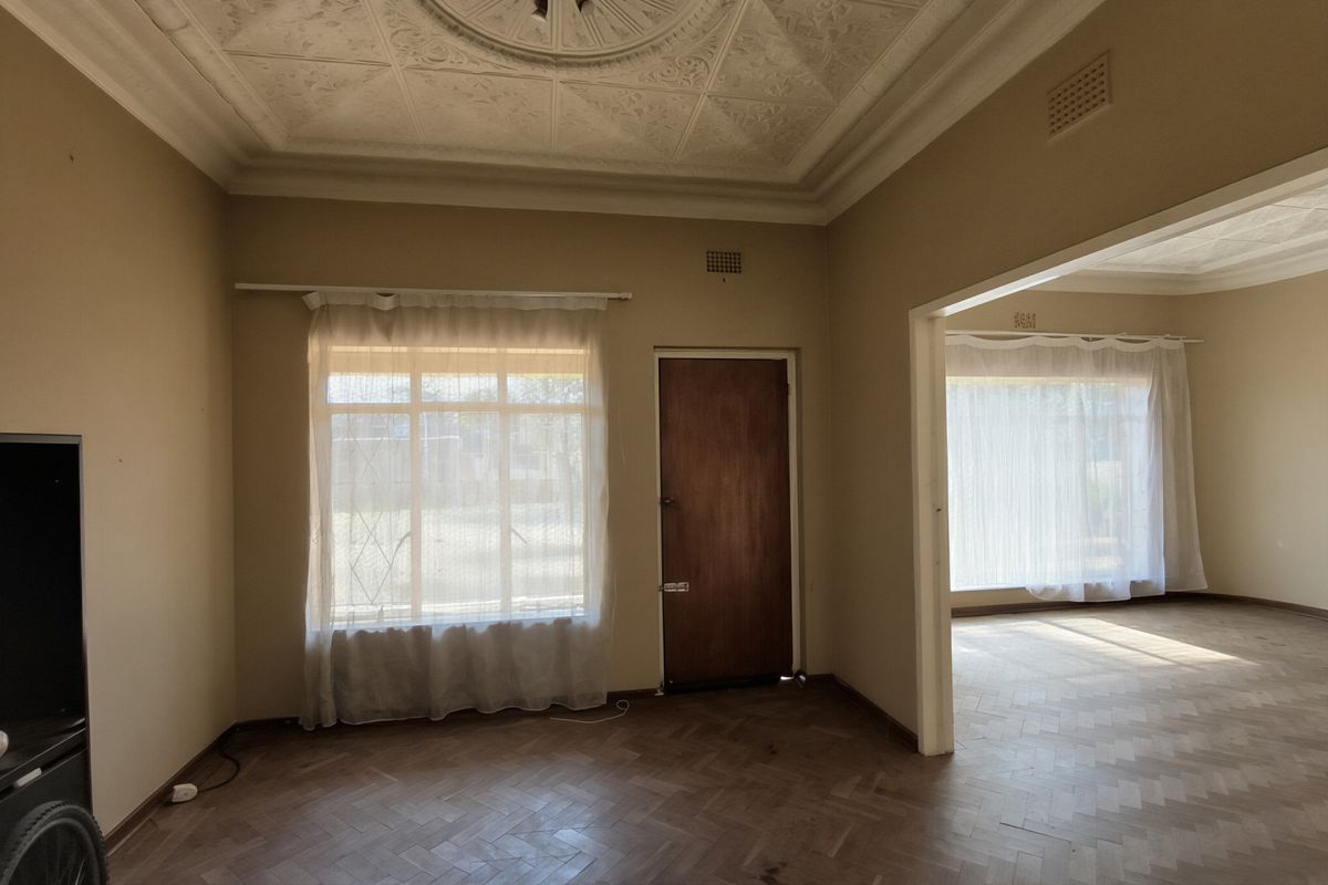 Spacious living area featuring original herringbone parquet flooring, ornate plaster ceiling detailing, and large windows allowing for ample natural light.