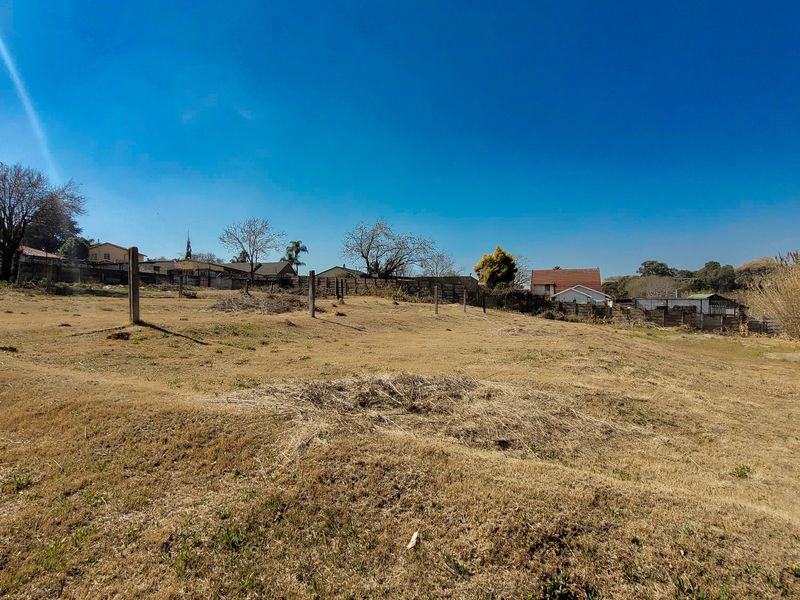 A large, undeveloped plot of land featuring dry grass, perimeter fencing, and wooden posts, offering potential for landscaping or future development.