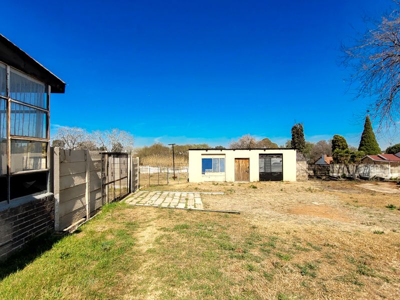 Rear yard view featuring a detached outbuilding, precast concrete boundary wall, and open grass area with paved access path.