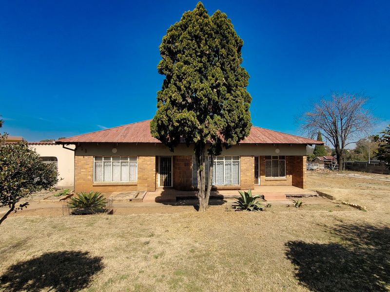 Front view of a single-story brick house featuring a covered porch, corrugated metal roof, and a spacious front garden area.