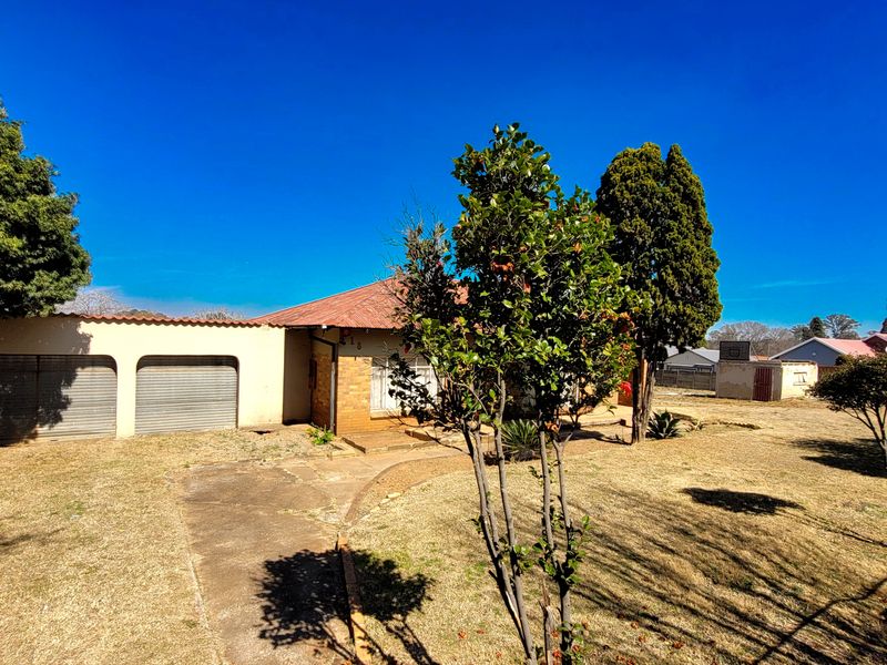 Front view of a single-story brick house featuring a double garage, tiled roof, and a large front yard with a concrete driveway.