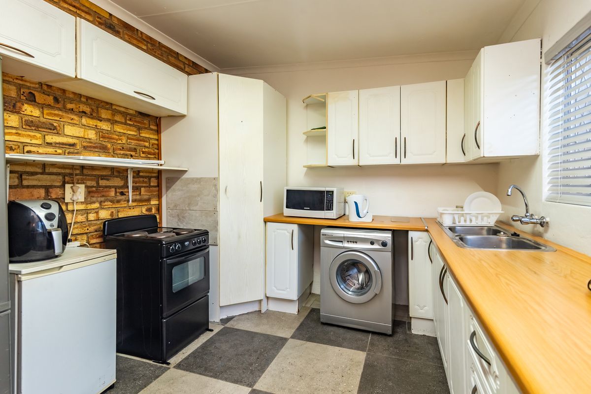 Functional kitchen featuring exposed brick walls, laminate countertops, double basin sink, and ample built-in cabinetry with tiled flooring.