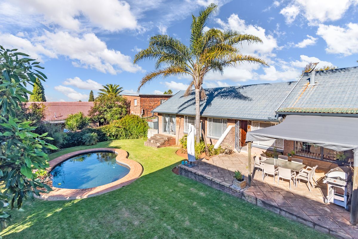 Rear exterior view featuring a landscaped garden, swimming pool, and a paved patio area with a covered outdoor entertainment space.