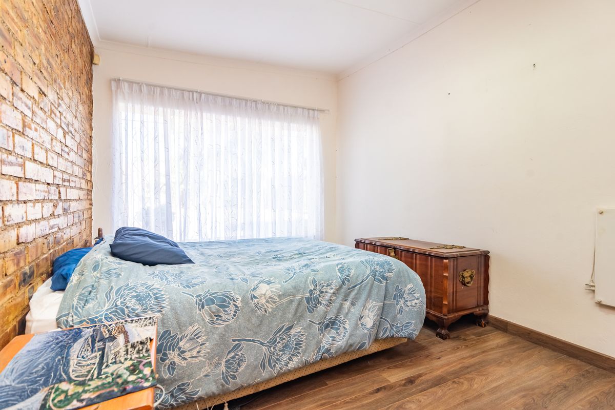 A bedroom featuring a distinctive exposed brick feature wall, laminate flooring, and a large window with sheer curtains.