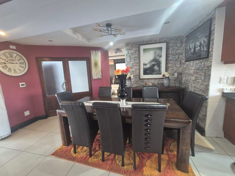 A dining room featuring a stone veneer accent wall, tiled flooring, and a recessed ceiling with modern lighting.