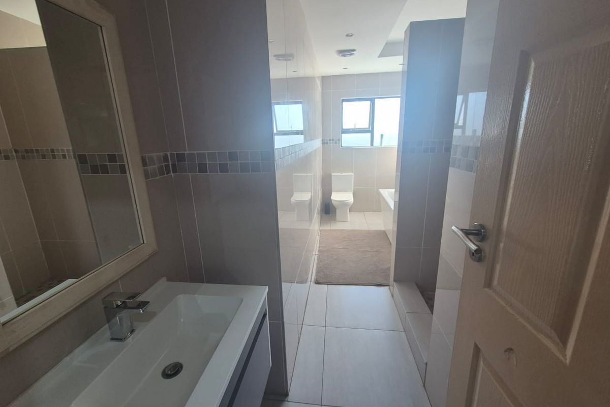 A modern bathroom featuring a vanity with basin, a toilet, and a bathtub, finished with neutral wall and floor tiles.