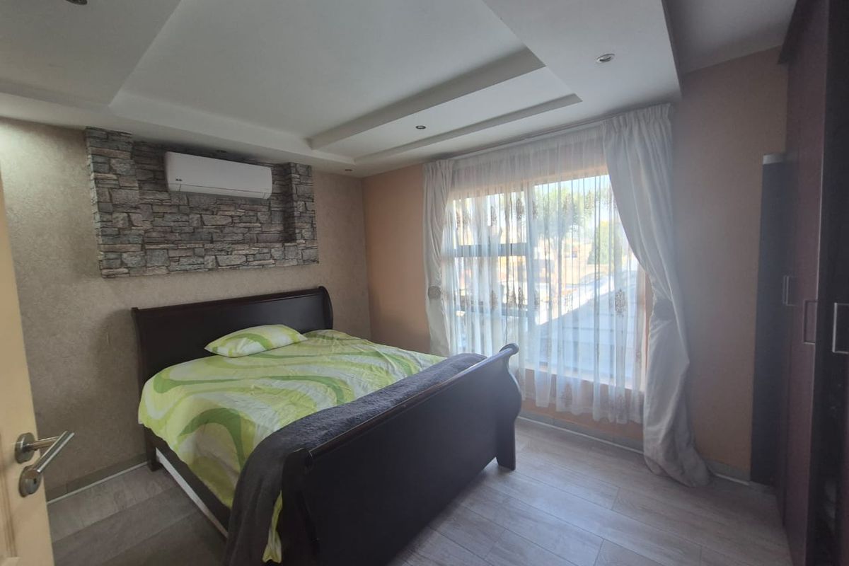 A well-maintained bedroom featuring a stone accent wall, recessed ceiling with downlights, split-system air conditioning, and laminate flooring.